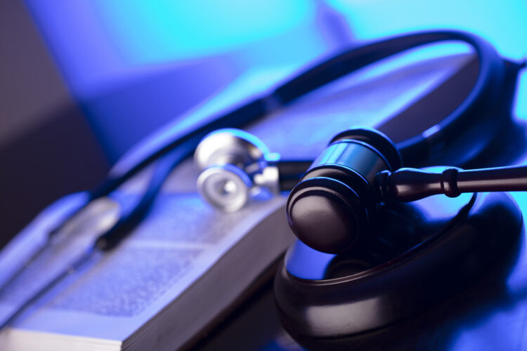 4 Factors Of Accepting Malpractice Settlement - Stethoscope and book on table blue background